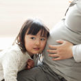 Child with ear against pregnant mother's stomach