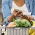 Closeup of person using a smart phone while pushing a grocery store shopping cart with food in it