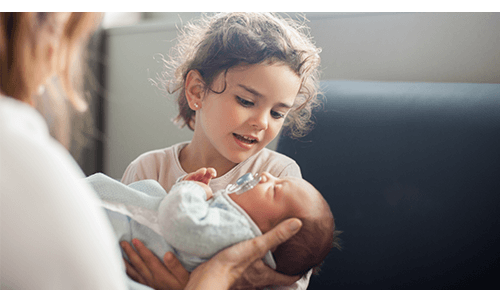 Child being helped by adult in holding infant Child being helped by adult in holding infant