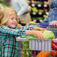 Child placing vegetable in a shopping cart at a grocery store