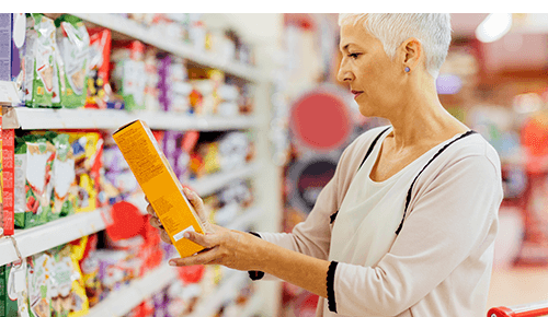 Woman reading nutrition label on box of food in grocery store aisle