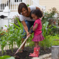 Adult and child using gardening equipment in small garden