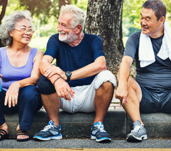 Three older adults sitting on curb after exercising