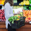 Person holding a shopping basket in the fruit aisle of a grocery store