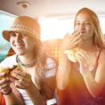 Three teenagers sitting in care together snacking on sandwiches