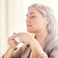 Relaxed looking person with eyes closed while listening to headphones and holding a cup of tea