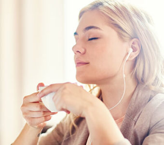 Relaxed looking person with eyes closed while listening to headphones and holding a cup of tea