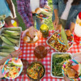 Overhead shot of potluck spread out on table with people around it