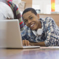 Teenager smiling and working on laptop computer while laying on the floor