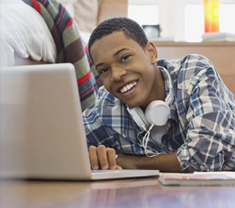 Teenager smiling and working on laptop computer while laying on the floor