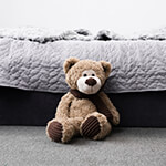 Stuffed teddy bear sitting on floor next to bed