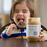 Child eating peanut butter out of the jar with a spoon