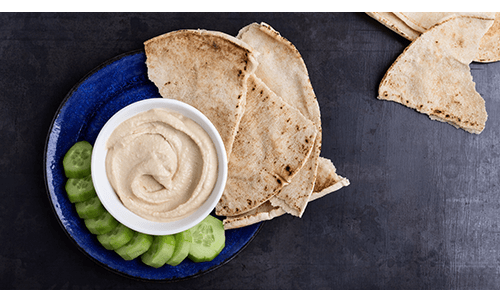 Pieces of pita and slices of cucumber next to a bowl of hummus