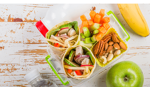 Lunchbox container with a vegetable wrap, cut up raw veggies and nuts