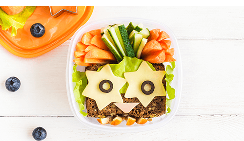 Container with sandwich and cut vegetables decorated to look like an animal