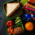 Several lunchbox containers with a variety of healthy food and snacks sitting on top of a chalkboard