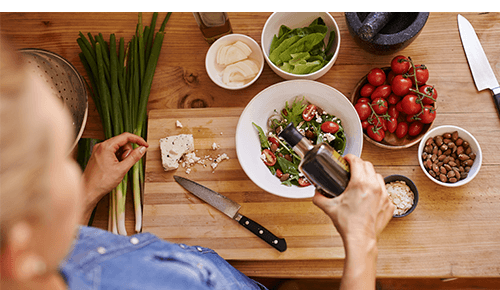 Person pouring olive oil over a bowl of salad and vegetables