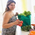 Woman unpacking fruits and vegetables from a shopping bag sitting on a kitchen counter