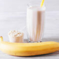 Blender cup with a protein shake sitting next to a measuring cup of protein powder and a banana
