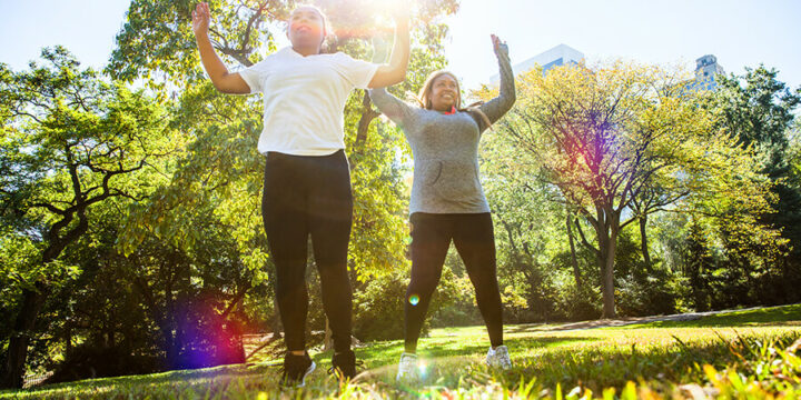 Mother and daughter doing jumping jacks and exercising outside in sun