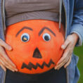 Closeup of pregnant person's stomach that is painted orange and decorated to look like a Halloween jack-'o-lantern