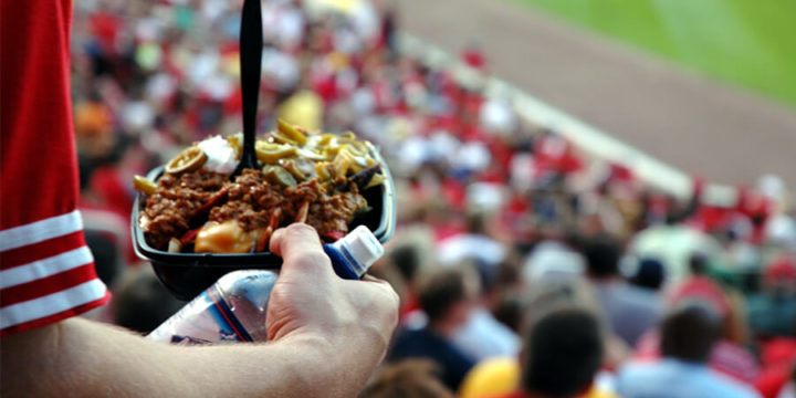 Closeup of person standing in packed sports stadium holding a plate of loaded nachos