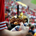 Closeup of person standing in packed sports stadium holding a plate of loaded nachos