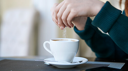 Person pouring sugar into cup of coffee 