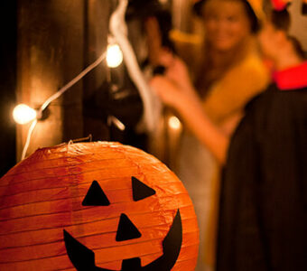 Jack-'o-lantern sitting on table with group in costumes in background