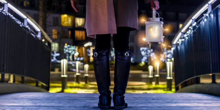 Person holding candle lantern on bridge with lights on it