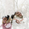 Two children smiling with arms out looking up at the snowflakes falling