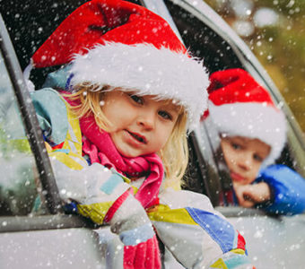 Children wearing Santa hats looking out the windows of a car