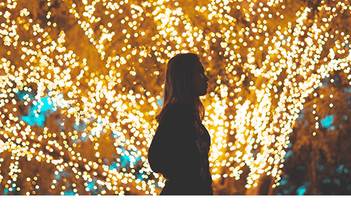 Woman walking by holiday lights in trees