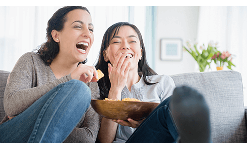 Friends laughing while watching a movie together and eating chips