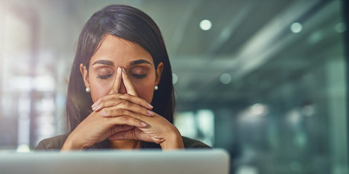 Person looking stressed and tired with hands at temple in front of computer