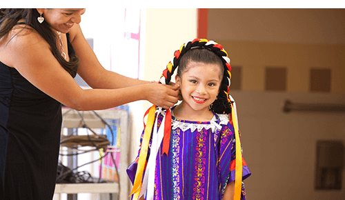 Woman putting a headband on a young child in traditional dress