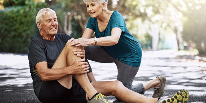 Woman helping injured man sitting on ground, holding knee in pain