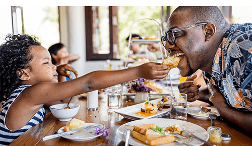 Small child feeding their father a piece of bread at a restaurant