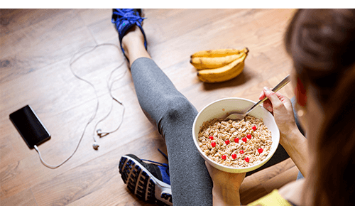 Person eating a healthy meal while sitting on ground next to mobile phone and a bunch of bananas