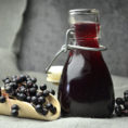 Bottle of elderberry syrup next to a scoop full of fresh elderberries on the vine