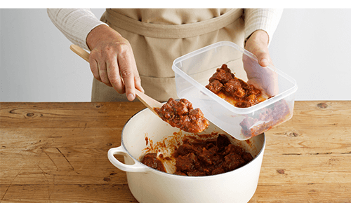 Person putting leftovers away from pot into plastic container