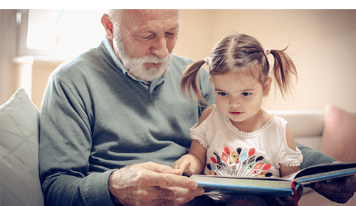 Grandfather holding grandchild in lap while reading a book to them
