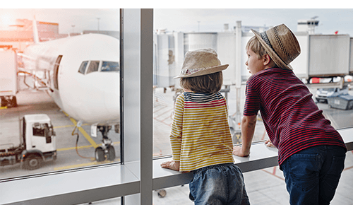 Two children standing at the window of an airport looking at airplanes Two children standing at the window of an airport looking at airplanes