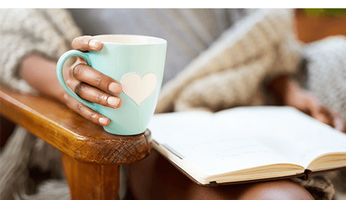 Closeup of a person holding a blue mug while reading a book