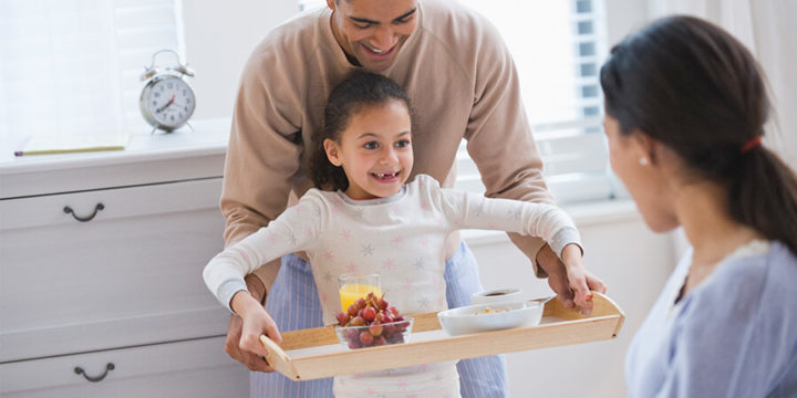 Father and daughter bringing a woman a breakfast in bed on a tray