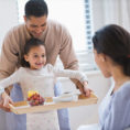Father and daughter bringing a woman a breakfast in bed on a tray