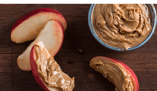 Slices of apple with nut butter on them next to a bowl of nut butter