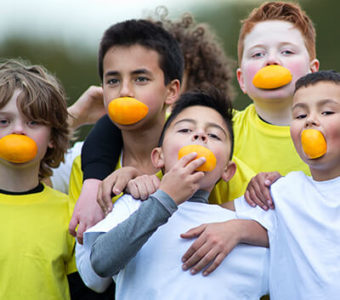 Group of young children holding each other and smiling with orange slices in their mouths