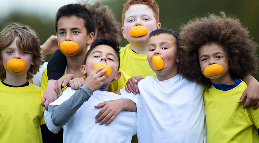 Group of children hugging and smiling with orange slices in their mouths Group of children hugging and smiling with orange slices in their mouths