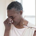Stressed looking person holding glasses while other hand is pinching the bridge of their nose